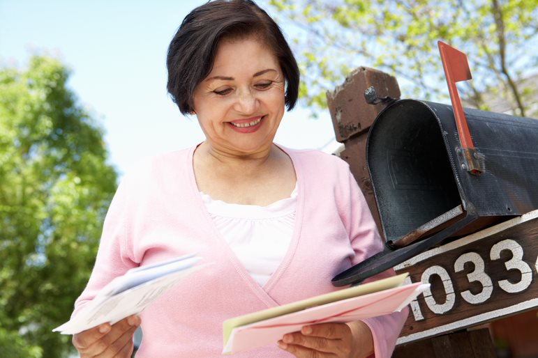 Smiling Senior Woman in a Pink Sweater Looking at Mail That She Got Out of Her Mailbox
