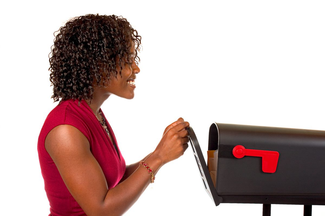 A Woman in a Red Shirt Smiles as She Gradually Opens Her Mailbox and Peers Inside